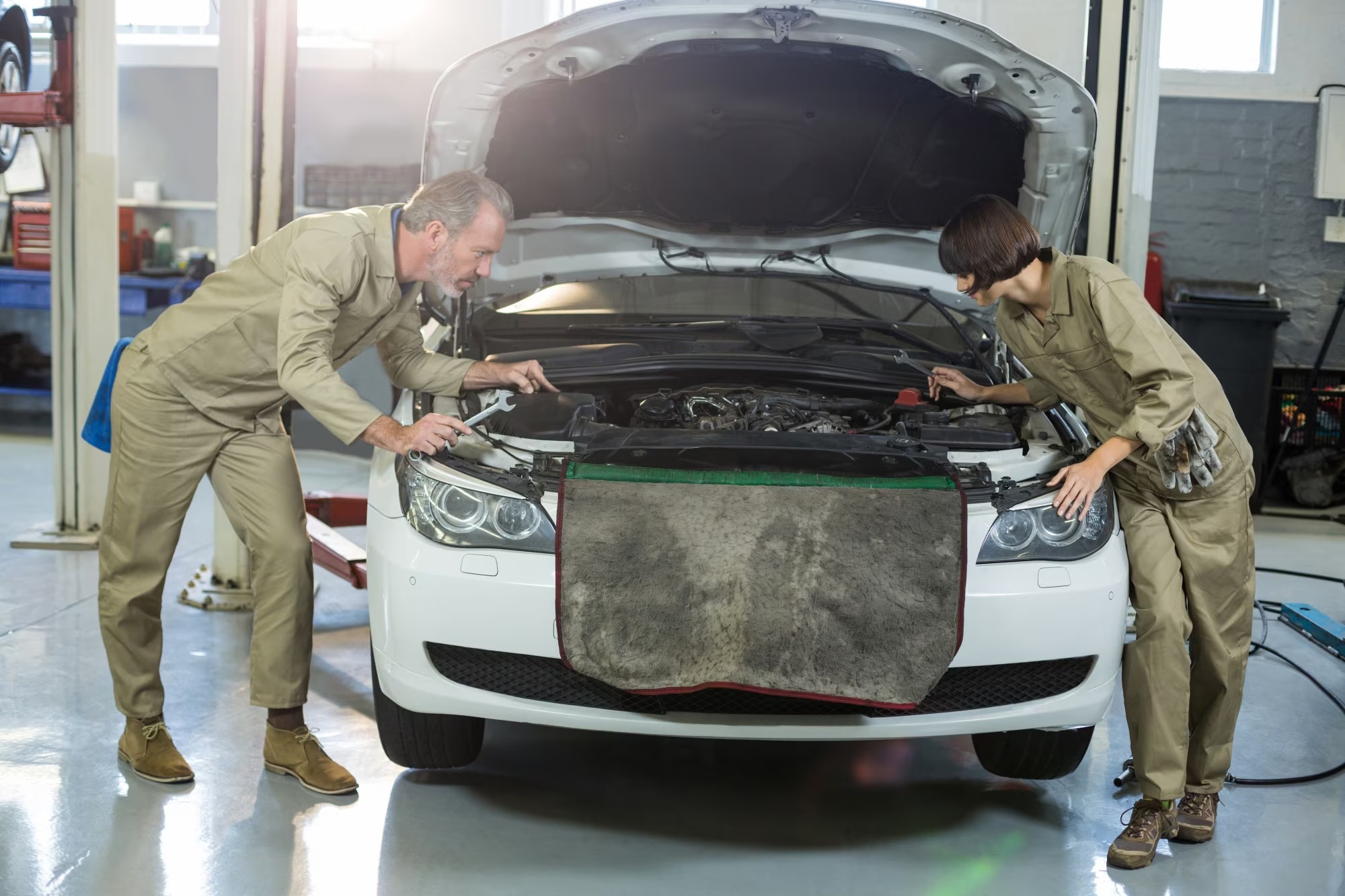 Auto Body Repair Services in Nicholasville KY 1 - Estes Pro Paint Two mechanics in beige coveralls inspect the engine with the car hood open in a white car inside an auto repair shop.