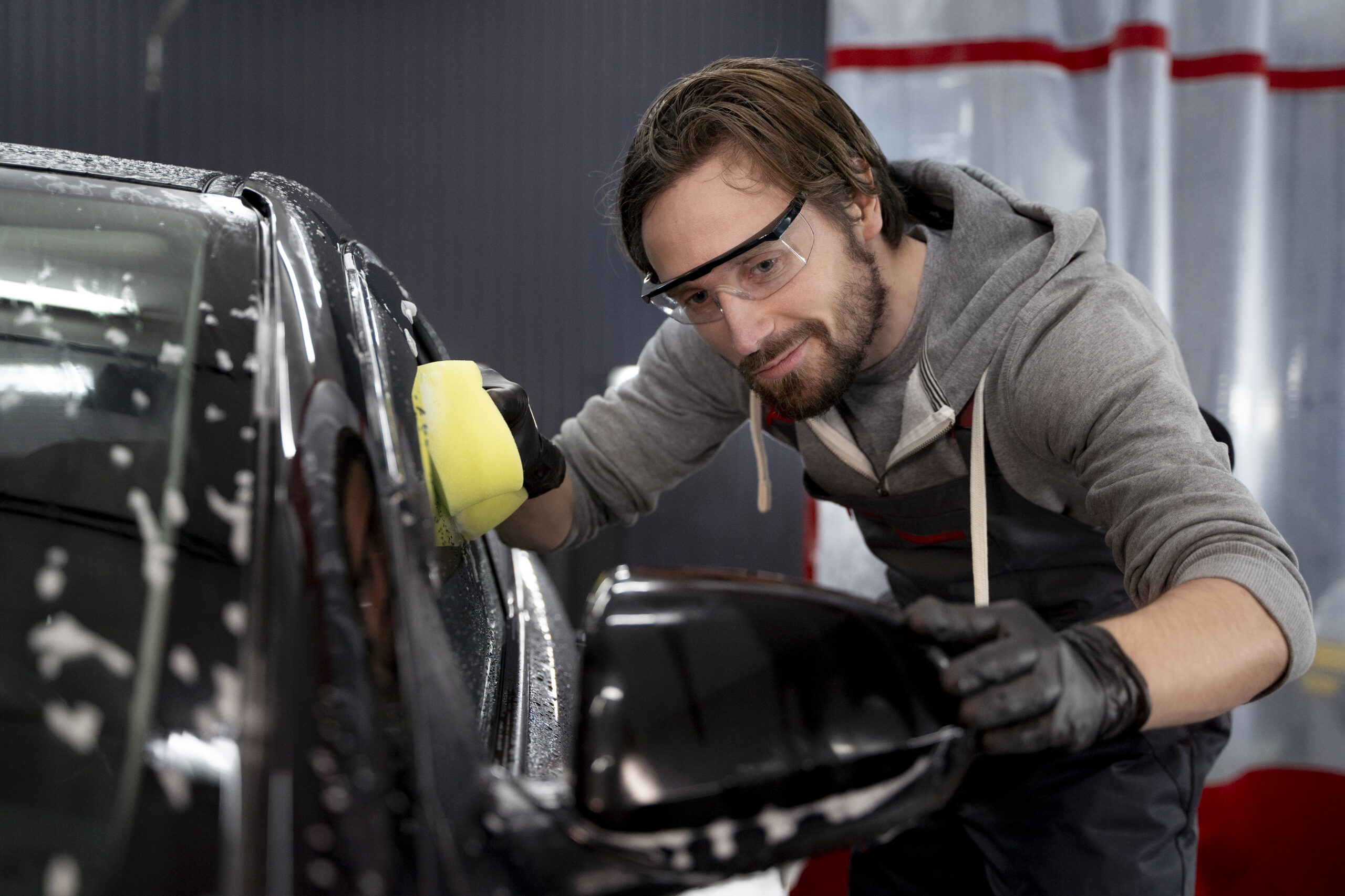 Auto Body Repair Services in Nicholasville KY 3 - Estes Pro Paint Auto detailer wearing safety glasses and gloves buffers a dark car with a yellow polishing pad.